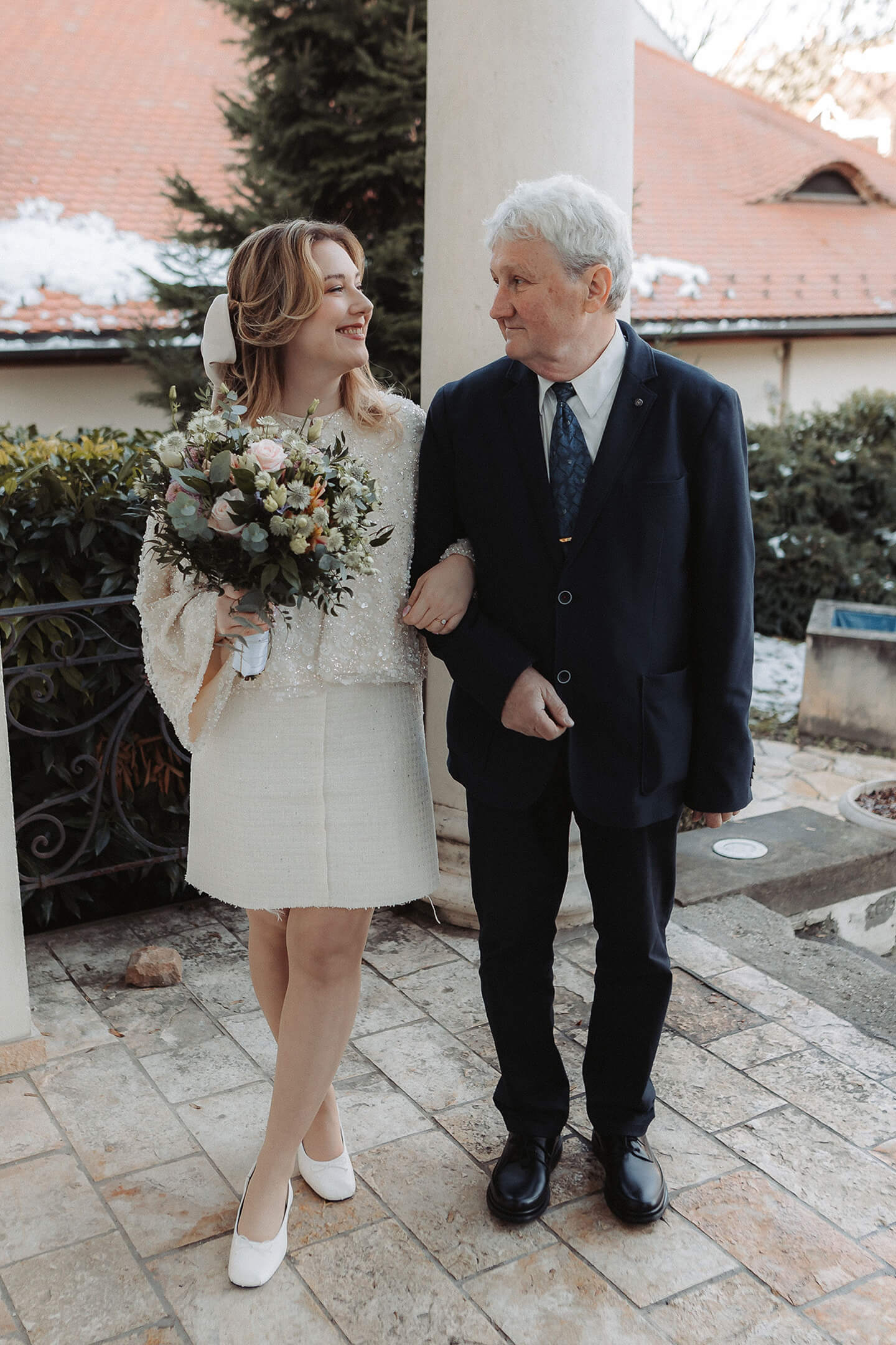 A bride and her father walk together, smiling, toward the wedding ceremony venue.