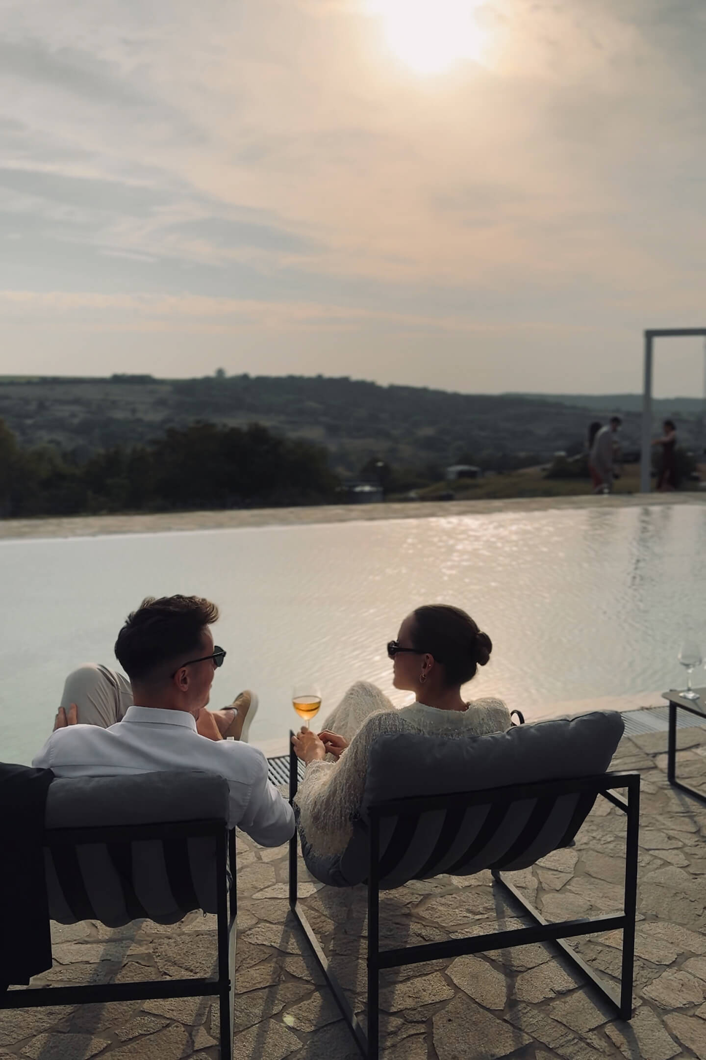 A couple sits by the poolside, watching the sunset.