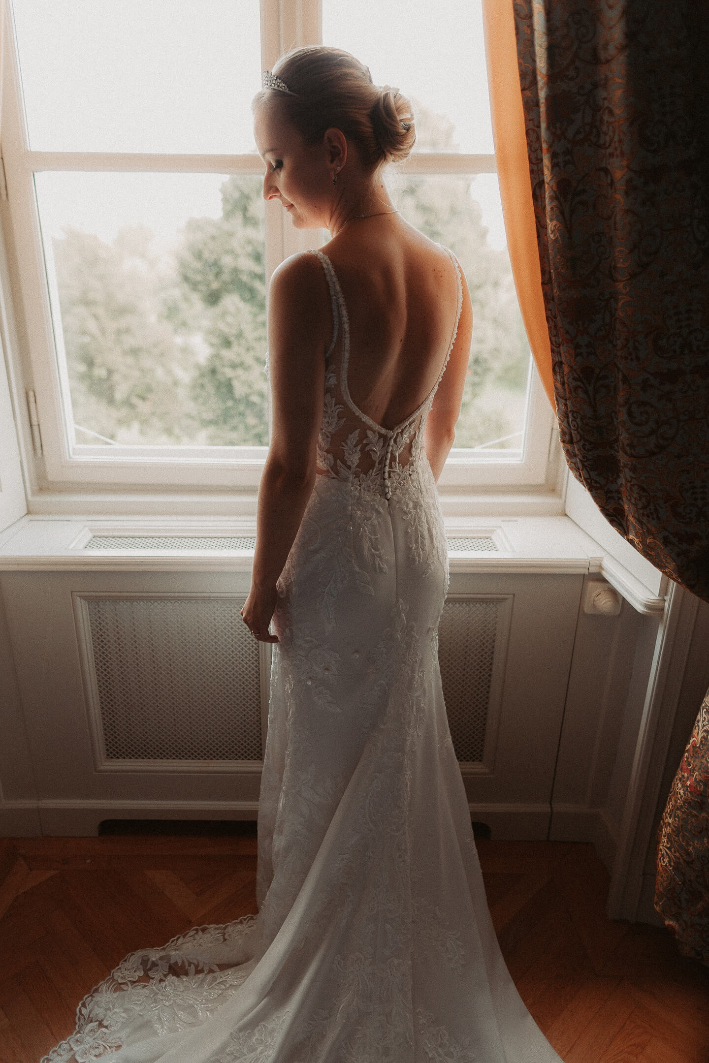 A bride stands in front of a large window, with natural light illuminating her dress.