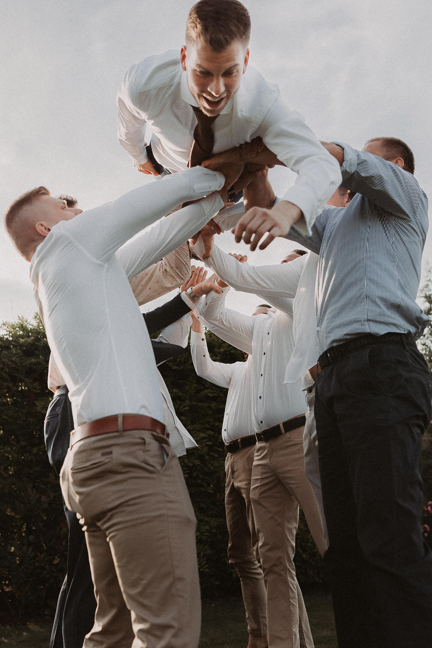 The groom smiles joyfully as his friends lift him into the air.