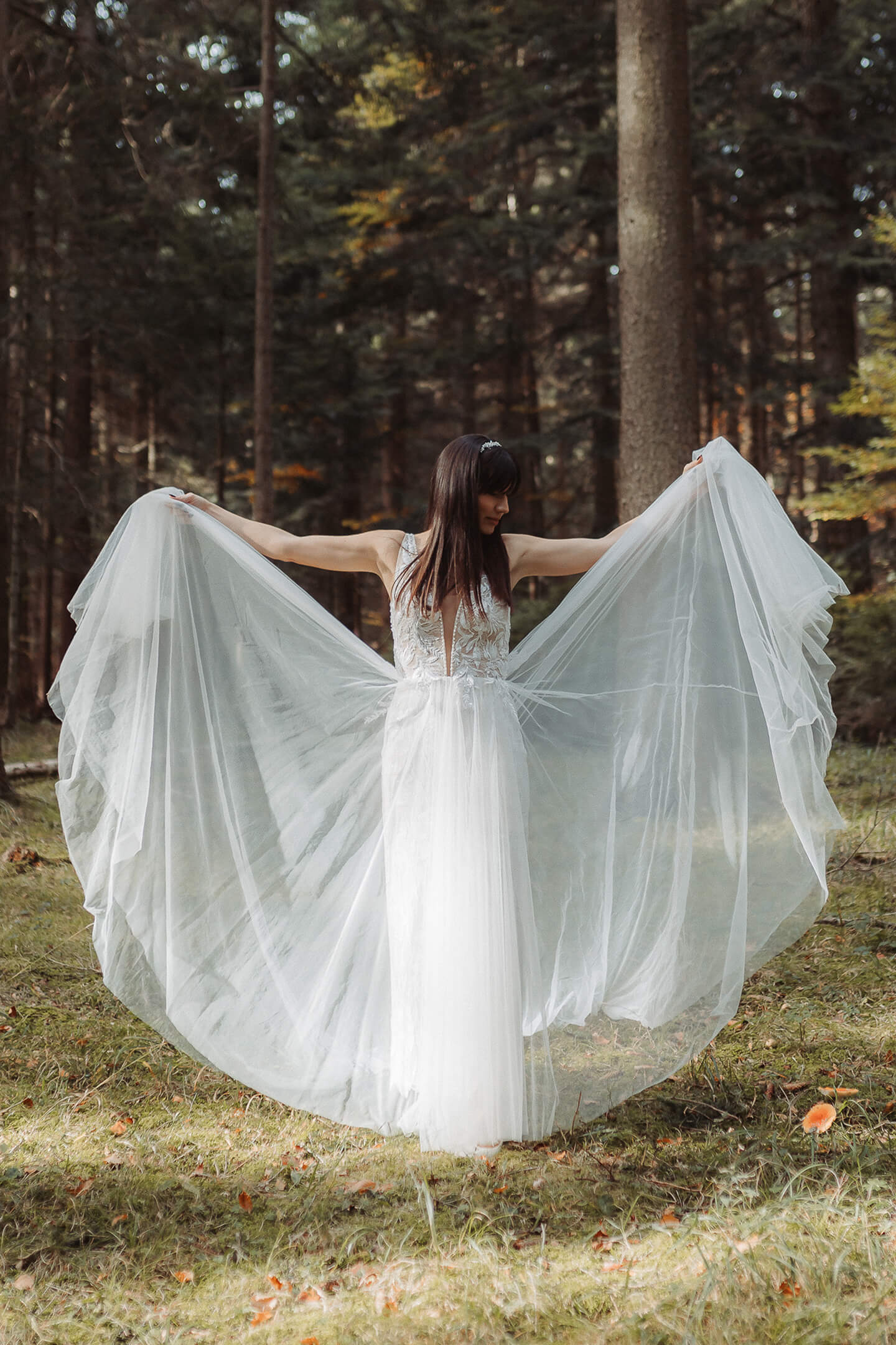 A bride stands in a forest clearing as her veil flows gracefully in the wind.