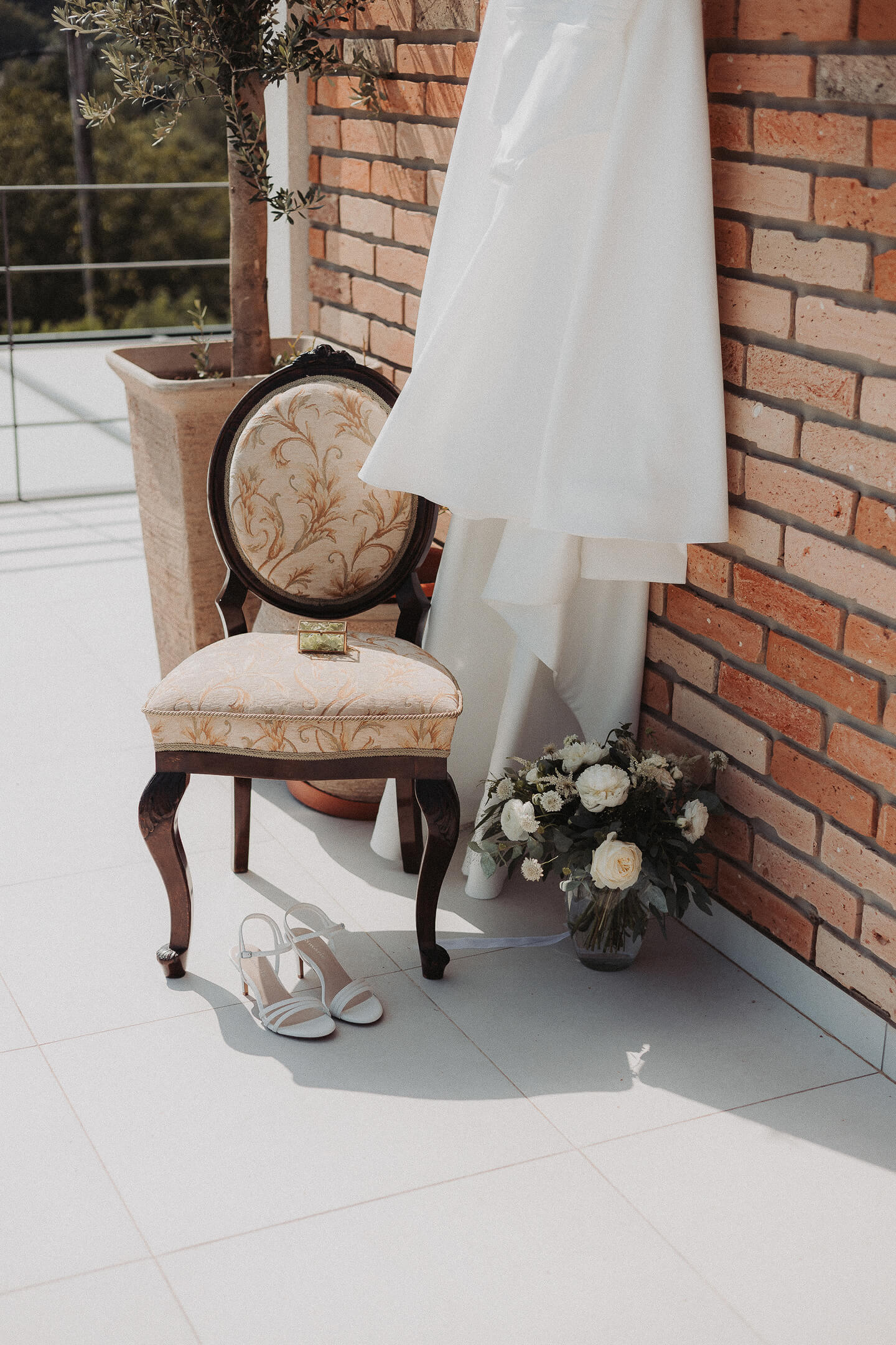 A vintage-style chair with a bridal shoe, a flower bouquet, and a small jewelry box placed on it.