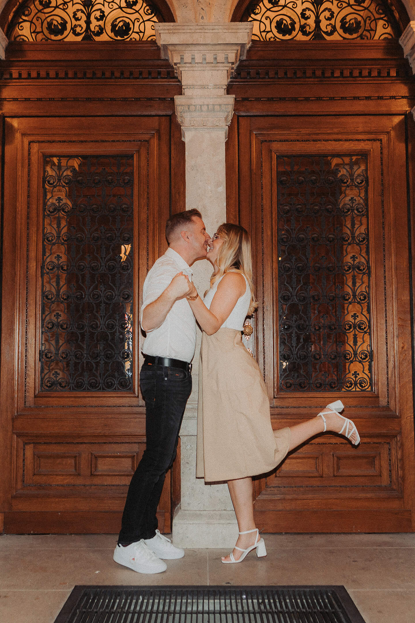 A loving couple shares a kiss in front of a beautiful wooden gate.